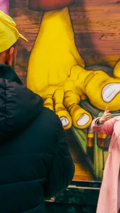 Guest viewing a large Os Gemeos mural
